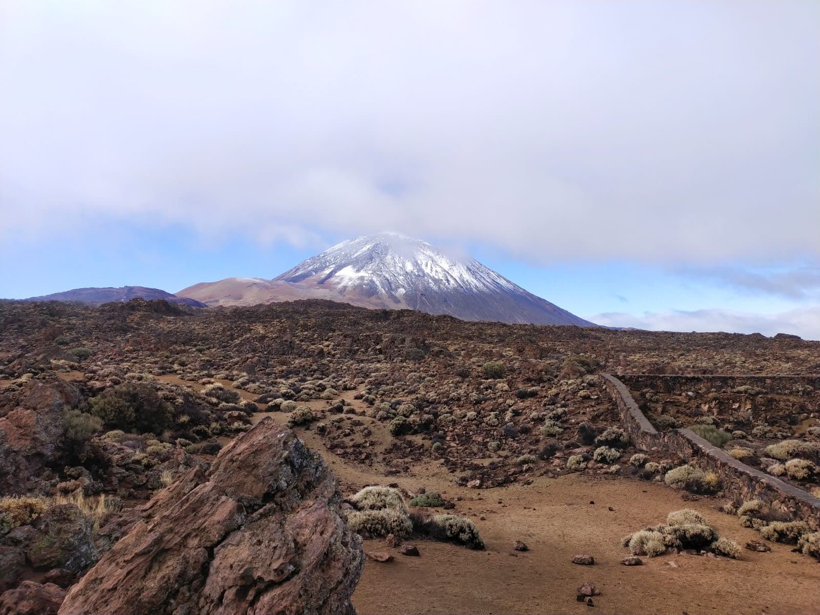 Vista del volcán Teide nevado sobre un paisaje volcánico árido y rocoso.